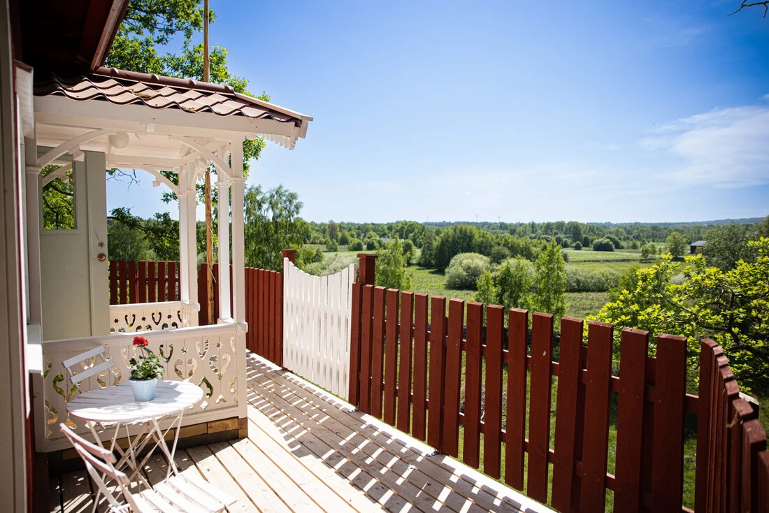 En solig dag på en veranda med vitt trästaket och en vacker utsikt över det grönskande landskapet på Mösseberg.