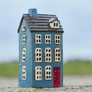 Blått keramikhus i form av ett townhouse med röd dörr och vita fönster, fotograferat utomhus.