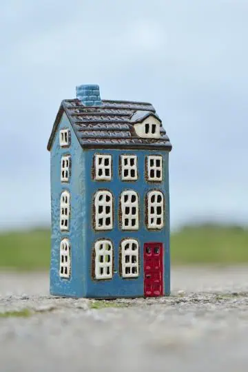Blått keramikhus i form av ett townhouse med röd dörr och vita fönster, fotograferat utomhus.