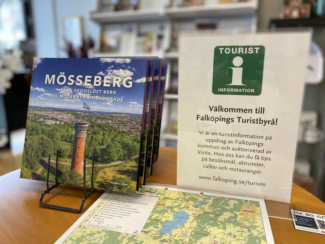 Informationsmaterial om Falköping och Mössberget i butikens turistinformation, med en tydlig välkomstskylt.
