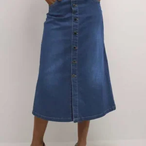Kvinna bär en blå midilång jeanskjol med knappstängning och fickor, stylad med vit topp och svarta klackar.