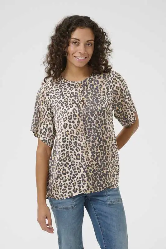 Kvinna bär en leopardmönstrad blus med kort ärm och knappdetalj, stylad med jeans i ljus tvätt.