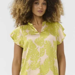 Kvinna bär en somrig blus med limegrönt monstera-mönster, kort fjärilsärm och V-ringning, stylad med matchande underdel.