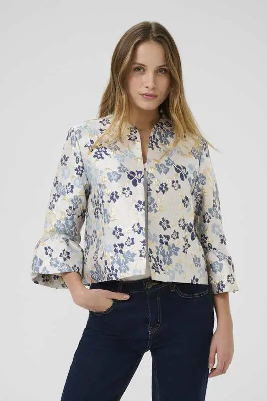 Kvinna bär en blommig jacka i skimrande jacquard med trumpetärmar och rak passform, från Culture.
