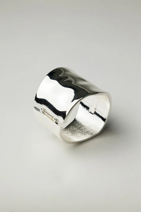 Brett hamrat armband i silverfinish med mjuka former och blank yta, fotograferat mot vit bakgrund.