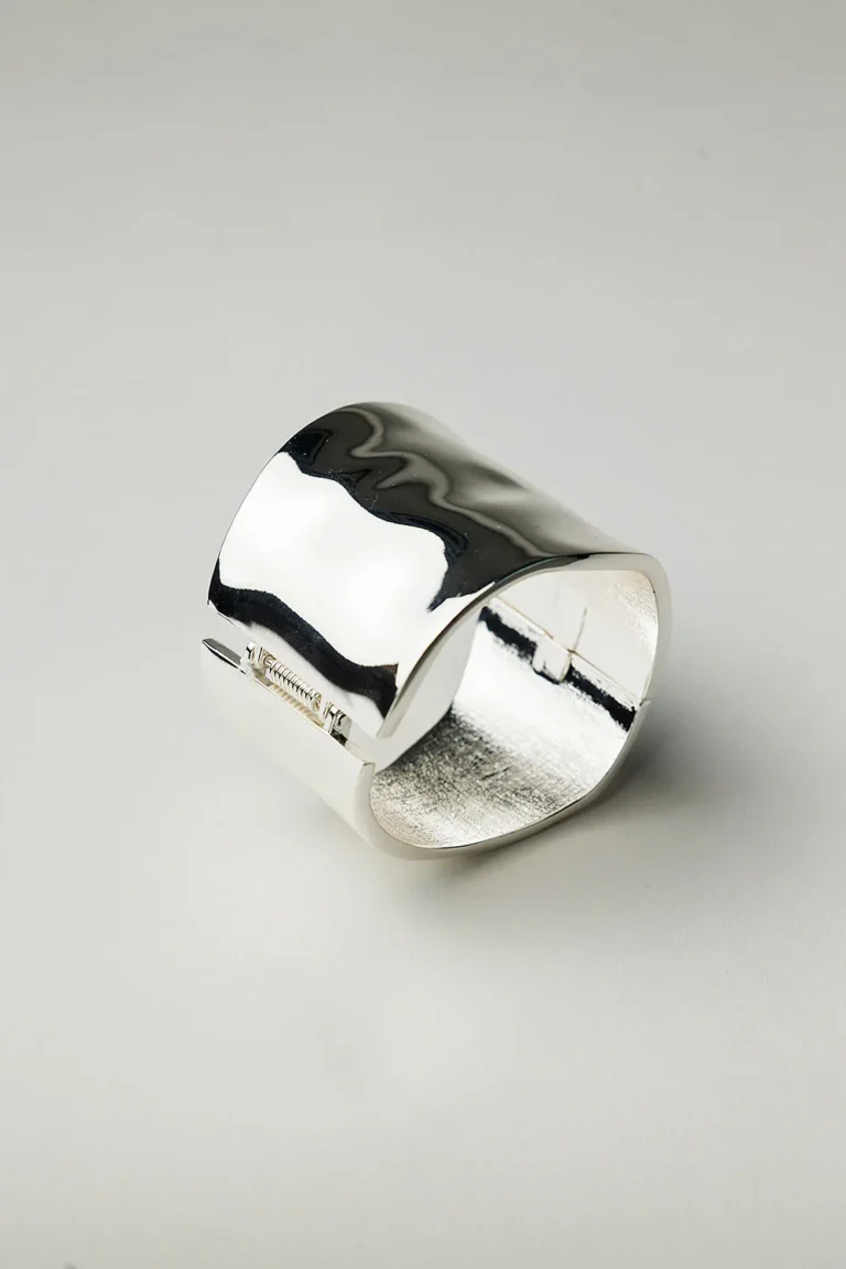 Brett hamrat armband i silverfinish med mjuka former och blank yta, fotograferat mot vit bakgrund.