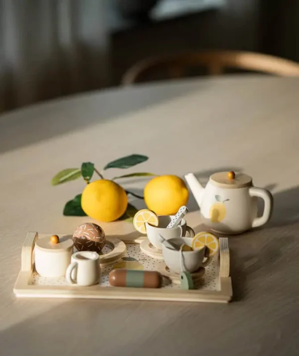 Jabadabado afternoon tea-set i trä uppdukat med tekanna, koppar, citroner och bakverk på ett ljust bord i naturligt solljus.