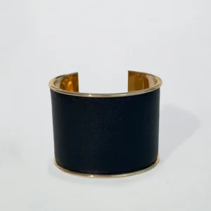 Svart manschettarmband med guldfärgade kanter och öppen design, elegant och modernt mot vit bakgrund.