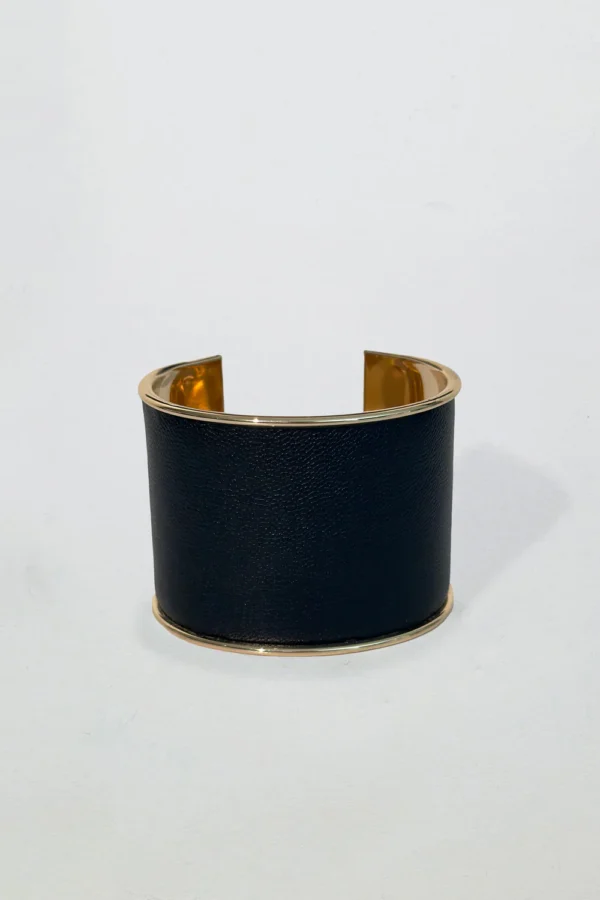 Svart manschettarmband med guldfärgade kanter och öppen design, elegant och modernt mot vit bakgrund.