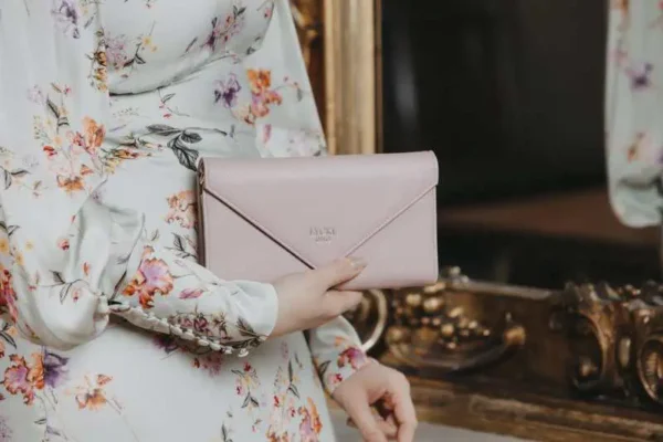 Rosa flap bag i kuvertmodell med silverkedja och justerbar rem, från Lycke Oslo – hänger fritt mot ljus bakgrund.