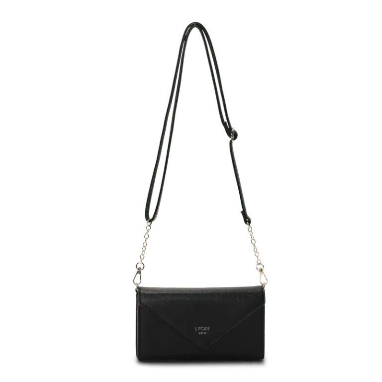 Svart flap bag i kuvertmodell med silverkedja och justerbar rem, från Lycke Oslo – hänger fritt mot ljus bakgrund.