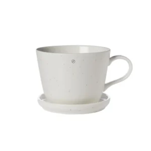 Kaffekopp med fat i vaniljfärgat porslin från ERNST, med rund form och mjuka detaljer, fotograferad mot vit bakgrund.