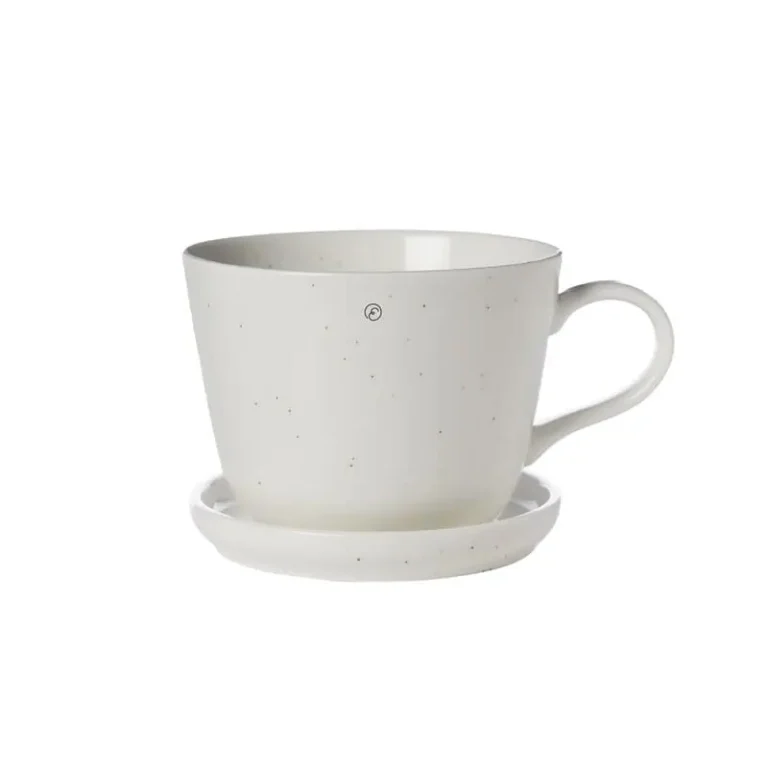 Kaffekopp med fat i vaniljfärgat porslin från ERNST, med rund form och mjuka detaljer, fotograferad mot vit bakgrund.