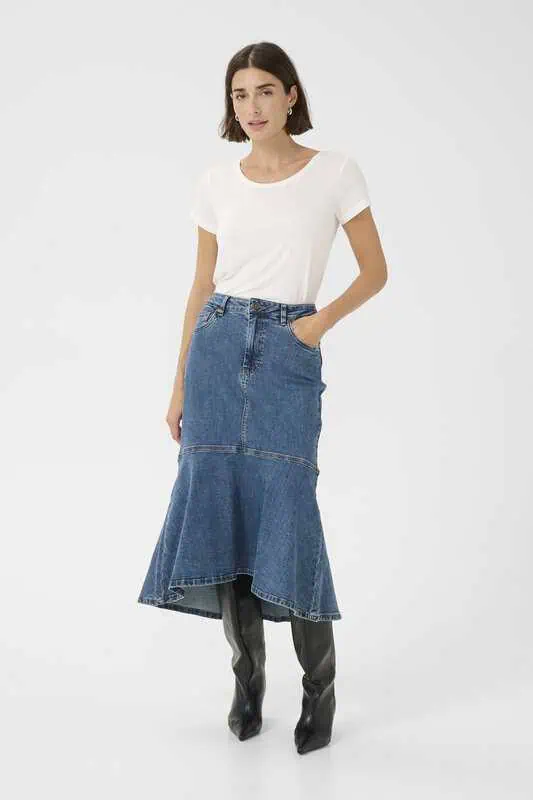 Kvinna i medelblå denimkjol med normal midja och utsvängd fåll, kombinerad med vit t-shirt och svarta stövlar.