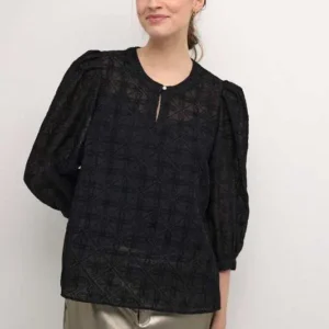 Kvinna i svart blus med strukturerat tyg, puffärmar och rund halsringning med liten öppning framtill.