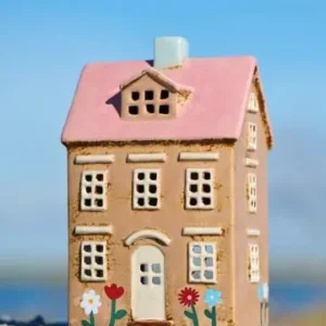 Keramikhus med rosa tak och målade blommor framtill, placerat i strandmiljö.