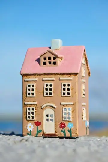 Keramikhus med rosa tak och målade blommor framtill, placerat i strandmiljö.
