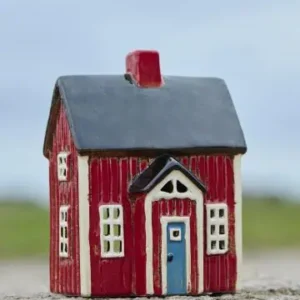 Rött keramikhus med blå dörr och vitt fönsterdetaljer, placerat utomhus på en stenig yta.