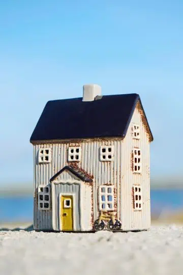 Keramikhus med svart tak, gult dörrparti och liten cykel framtill, placerat utomhus vid havet.