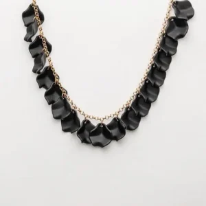 Leaf Mini Necklace i svart med bladformade detaljer på en tunn guldkedja, mot vit bakgrund.