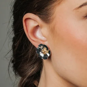 Blomformade örhängen i silver med gulddetaljer, liggande sida vid sida på ljusgrå yta.