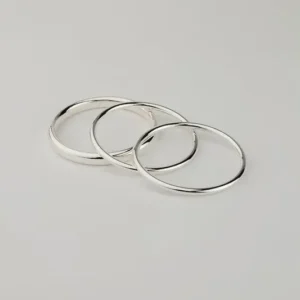 Set med tre tunna, silverpläterade armband i olika storlekar, placerade i ett överlappande mönster på vit bakgrund.