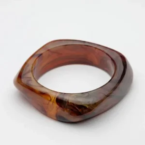 Armband i marmorerad brun och svart resin med fyrkantig form och rund insida, liggande på vit bakgrund.