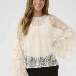 Kvinna iklädd cremefärgad spetsblus med volangärmar från Culture, stående avslappnat med händerna vid sidorna.