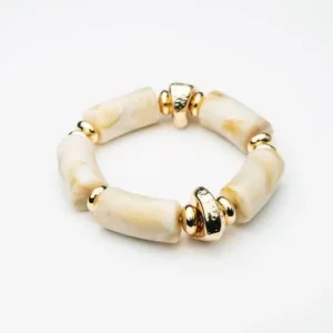 Armband med cylinderformade pärlor i naturvit resin och guldfärgade mellanringar, fotat ovanifrån på vit bakgrund.