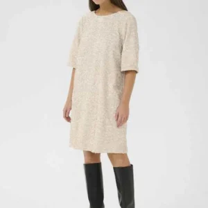 Kvinna i paljettklänning från Culture i champagnefärg, stylad med svarta höga stövlar.