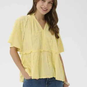 Modell bär gul blus från Culture med kort ärm, broderade detaljer och avslappnad passform tillsammans med jeans.