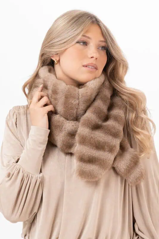 Kvinna med sandbeige Minerva Muffler fuskpälsscarf virad runt halsen över en ljus beige blus.