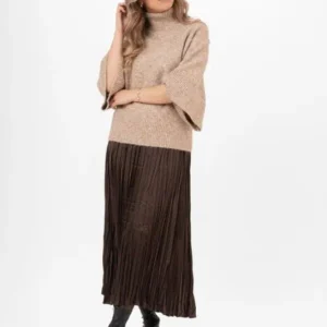 Modell i lång mörk plisserad satinkjol från Capri Collection, brun stickad polotröja och svarta boots mot vit bakgrund.