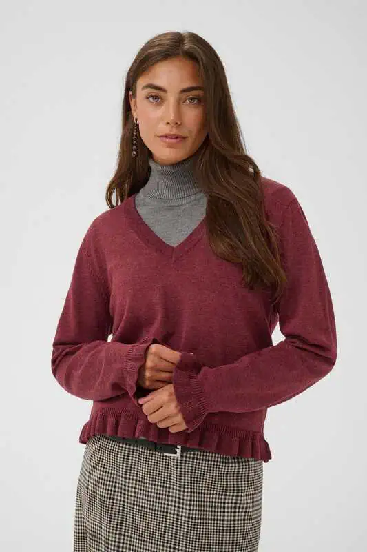 Modell i vinröd CUclare Annemarie Frill Vneck från Culture, en V-ringad stickad tröja med långa ärmar, volangdetaljer och ribbstickad nederkant.