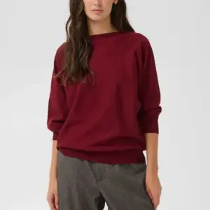 Modell i vinröd stickad CUannemarie Batwing Jumper från Culture med fladdermusärmar och oversize passform, matchad med grå byxor.
