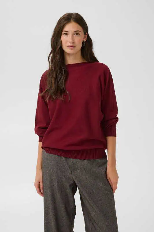 Modell i vinröd stickad CUannemarie Batwing Jumper från Culture med fladdermusärmar och oversize passform, matchad med grå byxor.