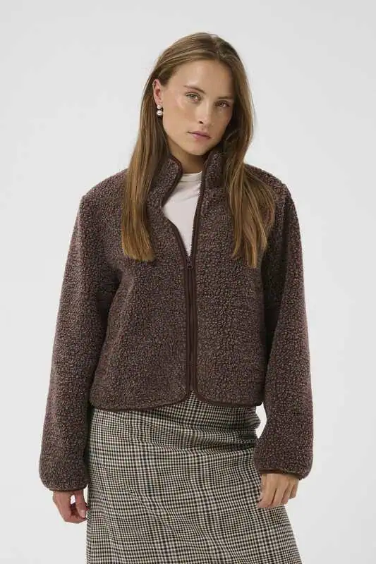 Modell i brunmelerad CUcatina Teddy Jacket från Culture med mjuk teddystruktur, hög krage, dragkedja och långa ärmar, matchad med rutig kjol.