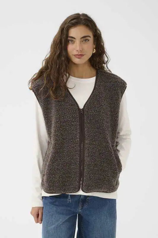 Modell i brunmelerad CUcatina Teddy Waistcoat från Culture med V-ringning, dragkedja och fickor, stylad med vit långärmad topp och blå jeans.